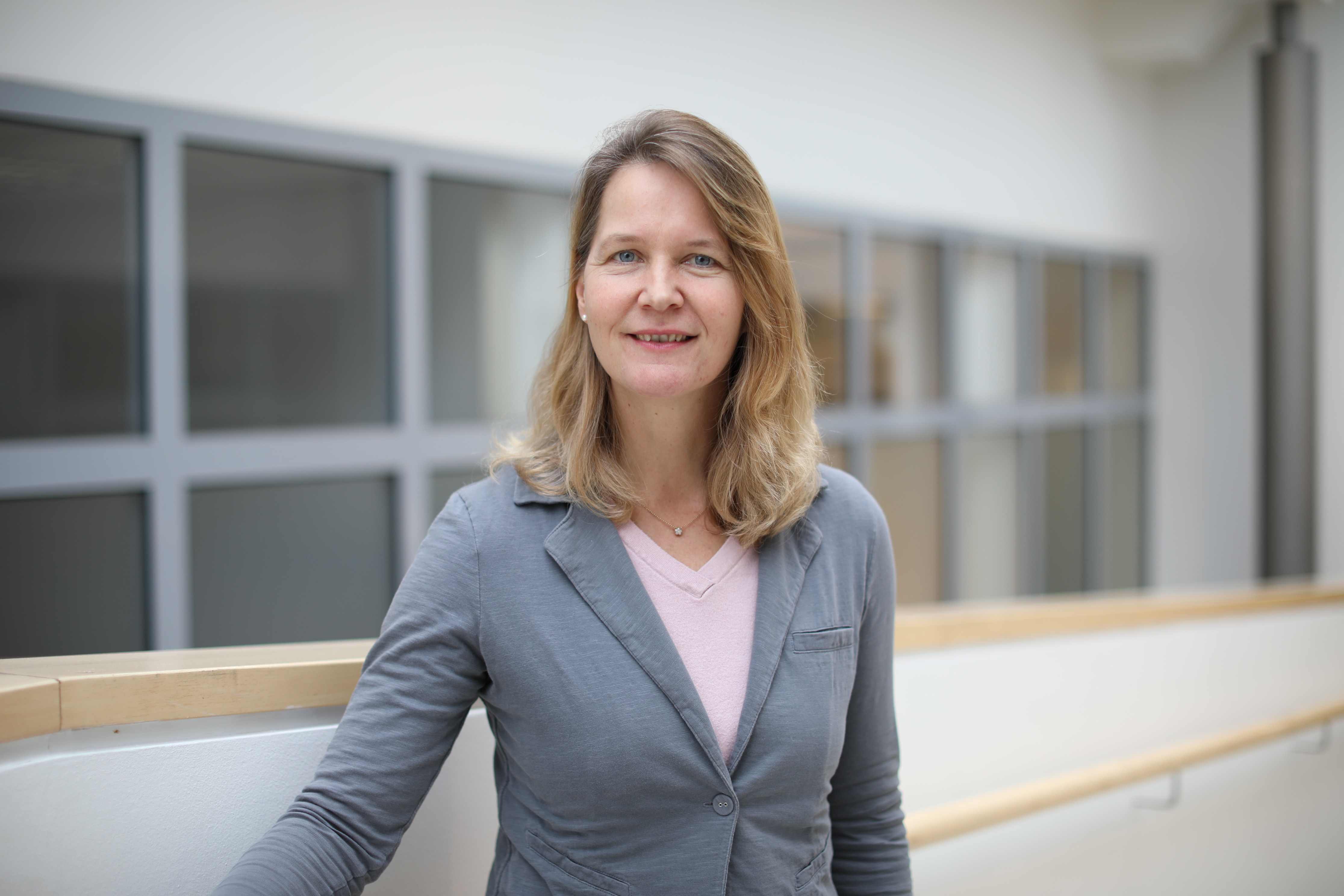 Weibliche Person in Alltagskleidung vor einem verschwommenen Hintergrund.