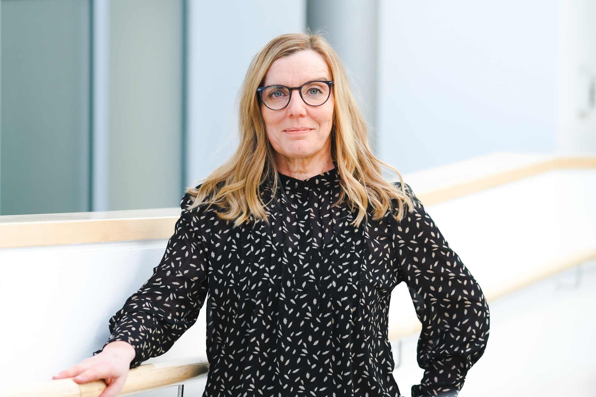 Weibliche Person in Alltagskleidung vor einem verschwommenen Fenster.