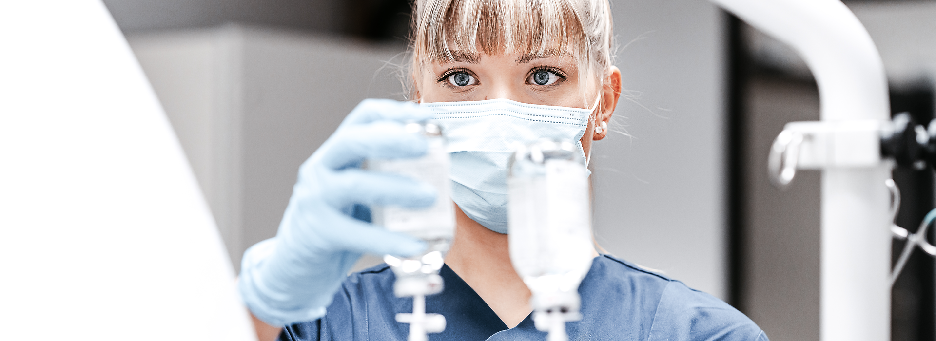 Medizinische Fachperson mit Mundschutz und Handschuhen bereitet Infusion vor