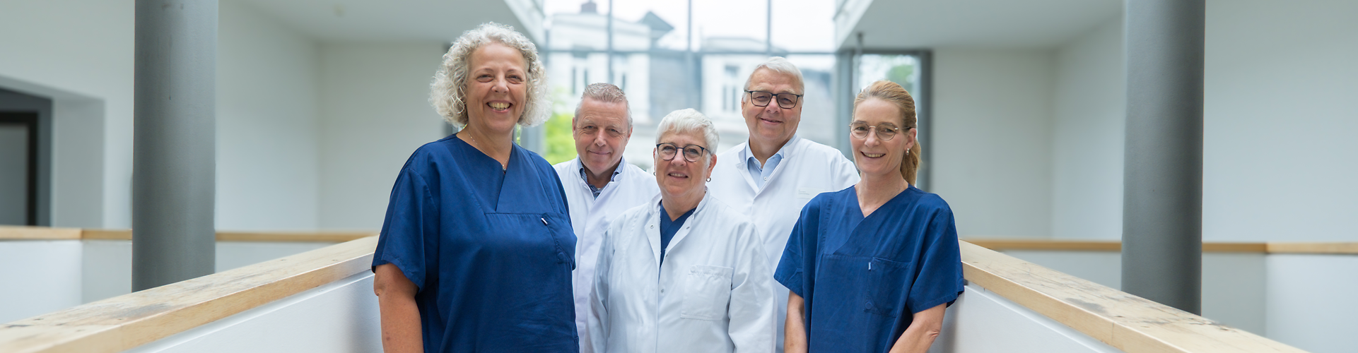 Fünf Personen, davon die äußeren beiden in blauem Kasack, die drei in der Mitte im weißen Kittel