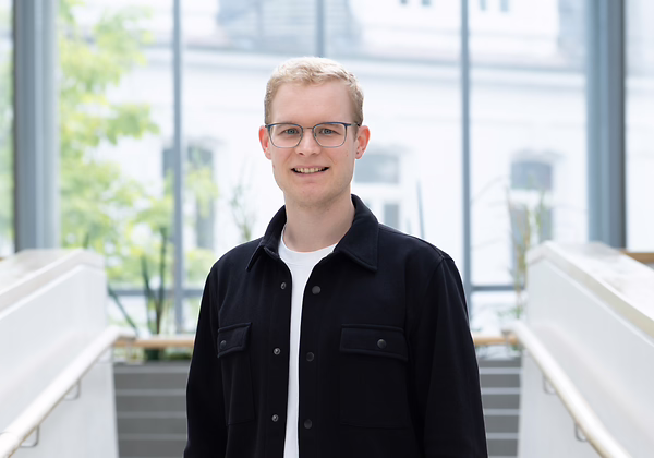 Männliche Person in Alltagskleidung vor einem verschwommenen Hintergrund.