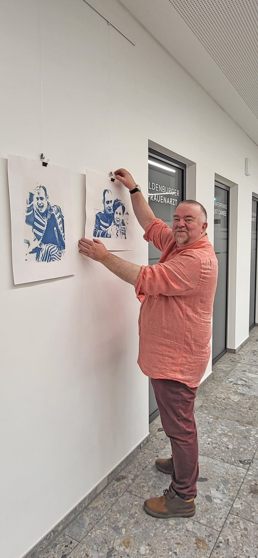 Mann in rosa Hemd vor zwei Fotografien